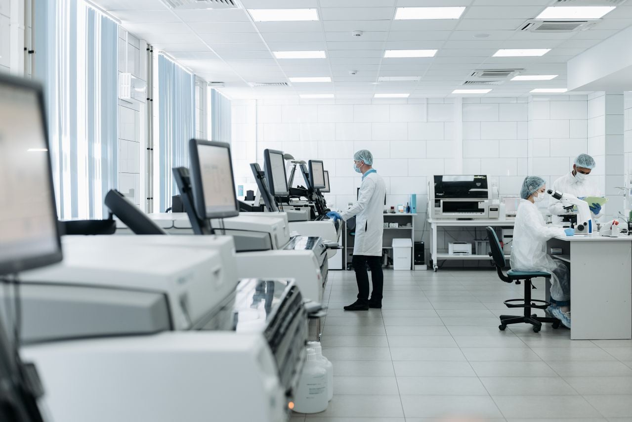 Three laboratory scientists conduct research in a lab equipped with complex computers and healthcare technology